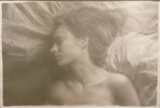 A woman laying on a sheet with her head turned to her right.