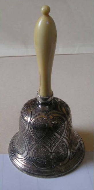 A silver dinner bell, engraved with floral design, and topped with an ivory handle.