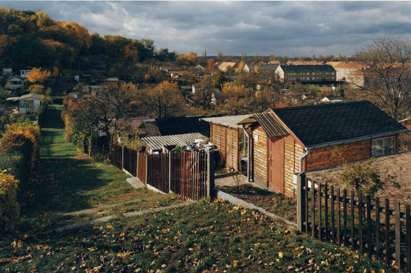 A photograph depicting an autumnal landscape featuring a grassy hill flanked by small houses be…