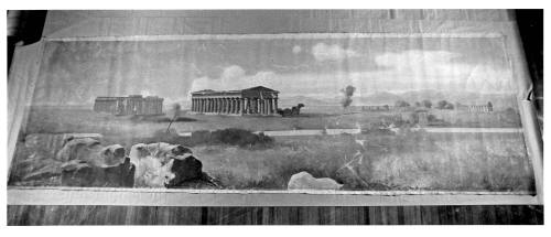 A horizontal landscape with grasses in the foreground, large rocks in the lower left, and Doric…