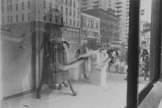 A black and white photograph of a Bloomingdale's store front window with mannequins, one standi…