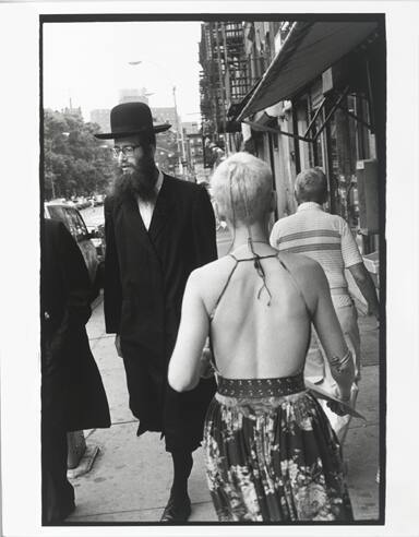 A black and white photograph of a blonde woman with her back to the camera in a floral printed …