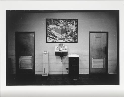 A black and white photograph of segregated drinking fountains between restrooms for "White Men"…