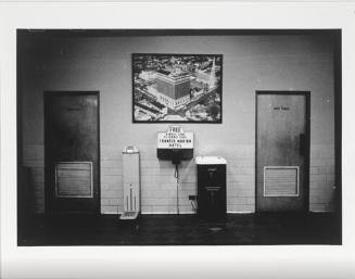 A black and white photograph of segregated drinking fountains between restrooms for "White Men"…