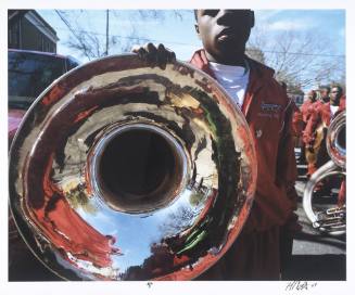 A photograph of a boy in a red marching band uniform holding a tuba reflecting the other band m…