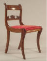 A Grecian-style klismos side chair with a red cushion decorated in a gold foliate design.