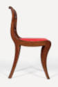 A side view of a Grecian-style klismos side chair with a red cushion decorated in a gold foliat…