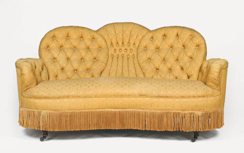 A Victorian settee upholstered in gold brocade with a tufted back and a fringe skirt. The sette…