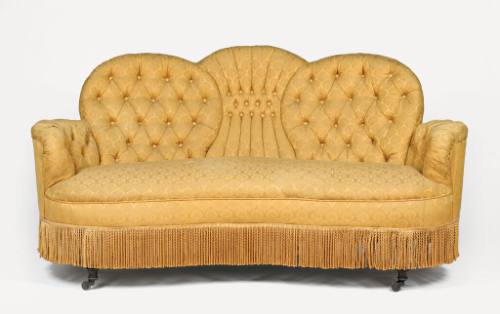 A Victorian settee upholstered in gold brocade with a tufted back and a fringe skirt. The sette…