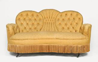 A Victorian settee upholstered in gold brocade with a tufted back and a fringe skirt. The sette…