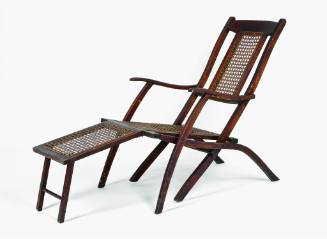 A wooden folding chair or chaise lounge deck chair with a caned back splat and seat.