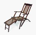 A wooden folding chair or chaise lounge deck chair with a caned back splat and seat.