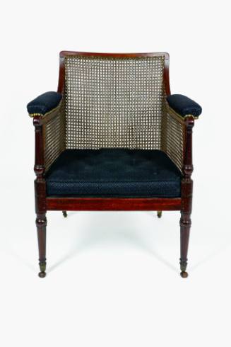 A mahogany armchair with caned back, sides, and seat supported by turned legs on casters. The a…