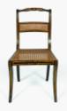 A frontal view of a black and gold fancy painted side chair with reeded crest rail and caned se…