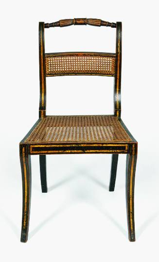 A frontal view of a black and gold fancy painted side chair with reeded crest rail and caned se…