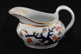 A cream pitcher from a twenty-one-piece tea service characterized by a tree and its base leaves…
