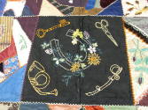 A detail of a patch with a horseshoe, key, sword, scissors, and a horn. 