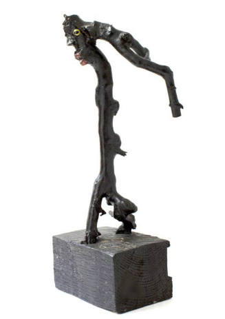 A sculpture comprised of a black painted stick with yellow eyes and red lips on a rectangular b…