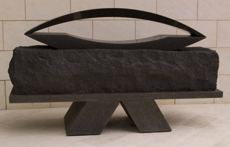 A black stone sculpture comprised of three textural surfaces in the form of a rectangular block…