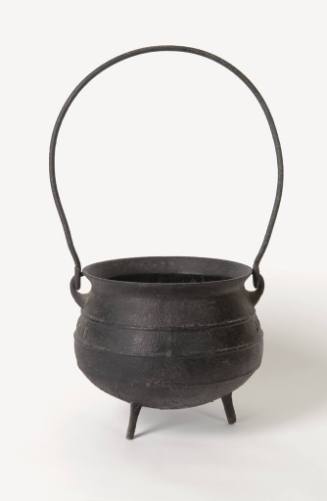 A cast iron, three-legged pot or cauldron with a tall handle, flared lip and narrow bands aroun…