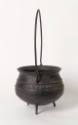 The side of a cast iron, three-legged pot or cauldron with a tall handle, flared lip and narrow…