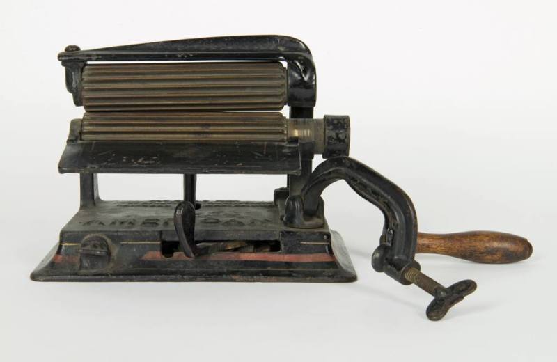 A cast iron fluting iron with a clamp, wooden handle and brass rollers.