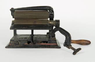 A cast iron fluting iron with a clamp, wooden handle and brass rollers.