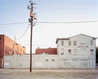 A utility pole bisects a large white building with hand painted signs.